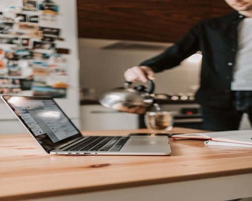 Seseorang menikmati secangkir teh panas sambil mengalihkan pandangan dari laptop